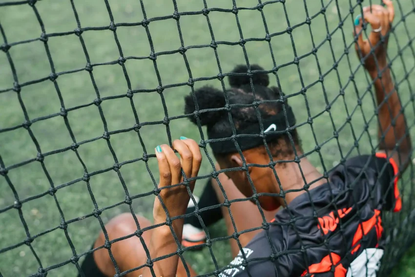 Les secrets d’entraînement des meilleurs athlètes 7 Jeune femme en tenue de sport, regardant à travers un filet de football.