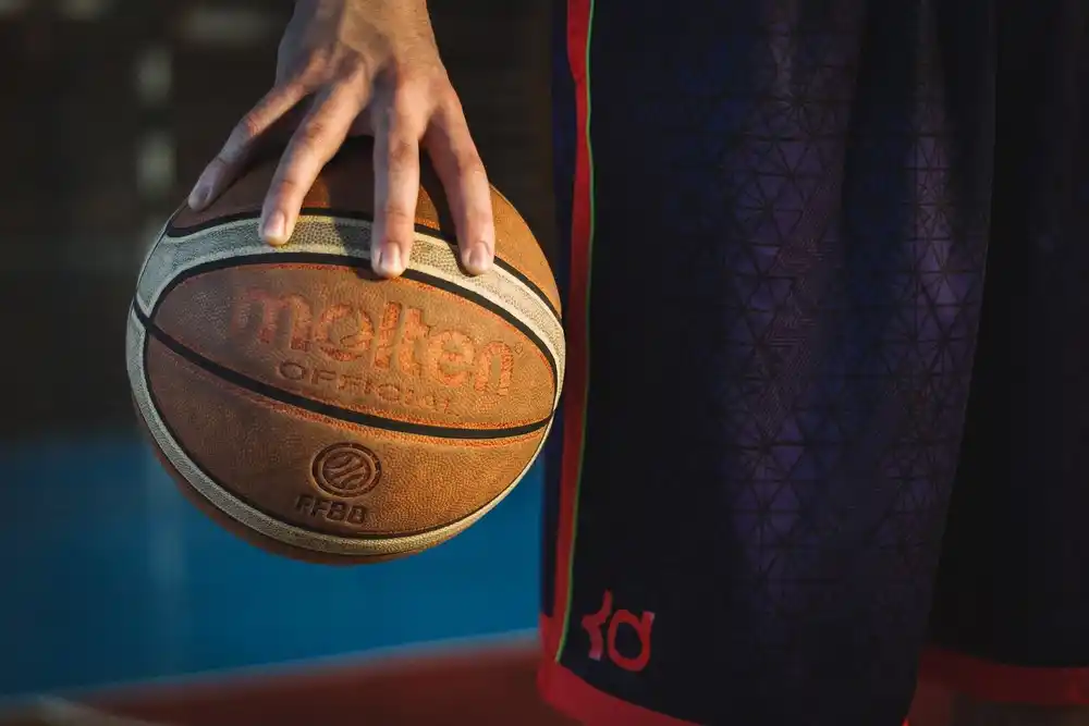 Les joueurs américains de basketball révélation de la saison NBA 2026 12 Main tenant un ballon de basketball sur un terrain avant un entraînement.