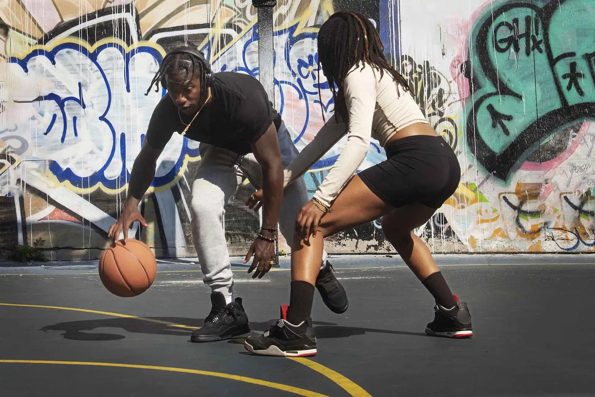 Basketball : comment le tir à trois points a transformé le jeu ? 2 Deux joueurs disputant un duel de basketball sur un terrain urbain en extérieur devant un mur de street art.