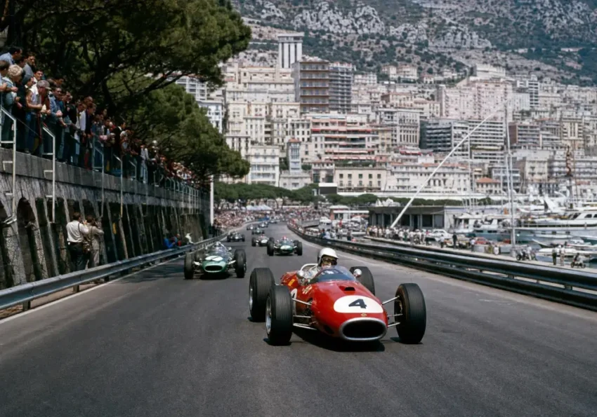 Une monoplace de Formule 1 roule devant des tribunes anciennes et des virages bordés de grillages.